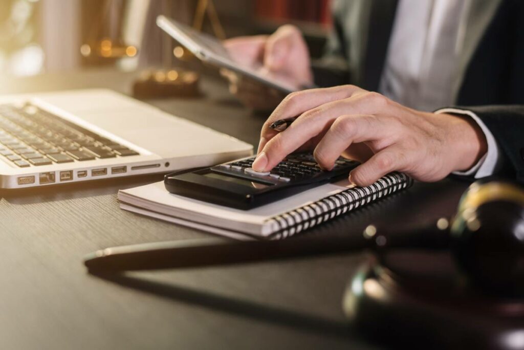 man sitting in front of a laptop and judge's gavel using a calculator